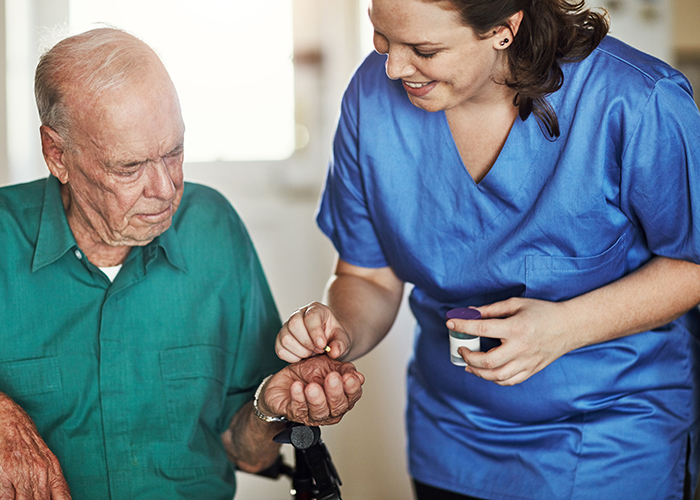 A female medication administration aid gives a patient his medicine.