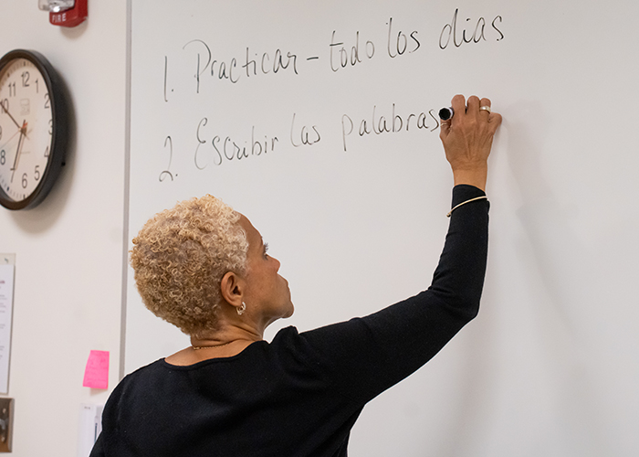 A female instructor writes medical terms in Spanish on a whiteboard.