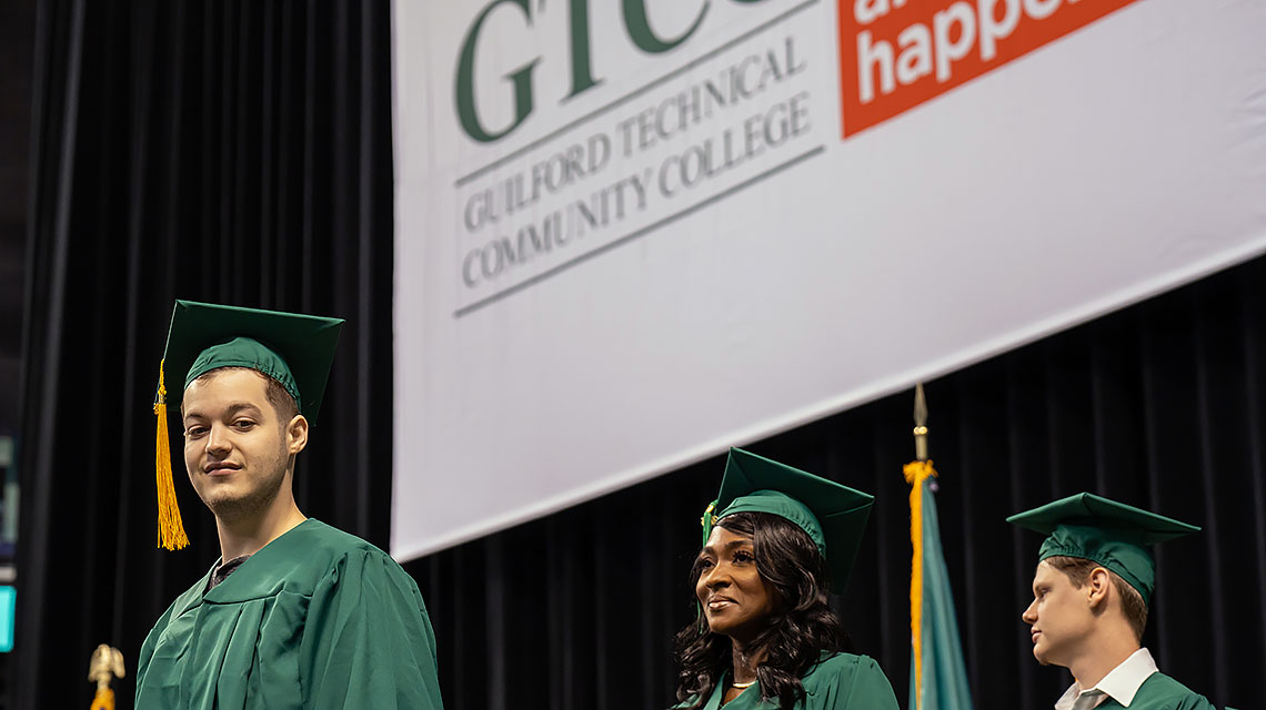 Three students look down from the presentation stage at the crowed.